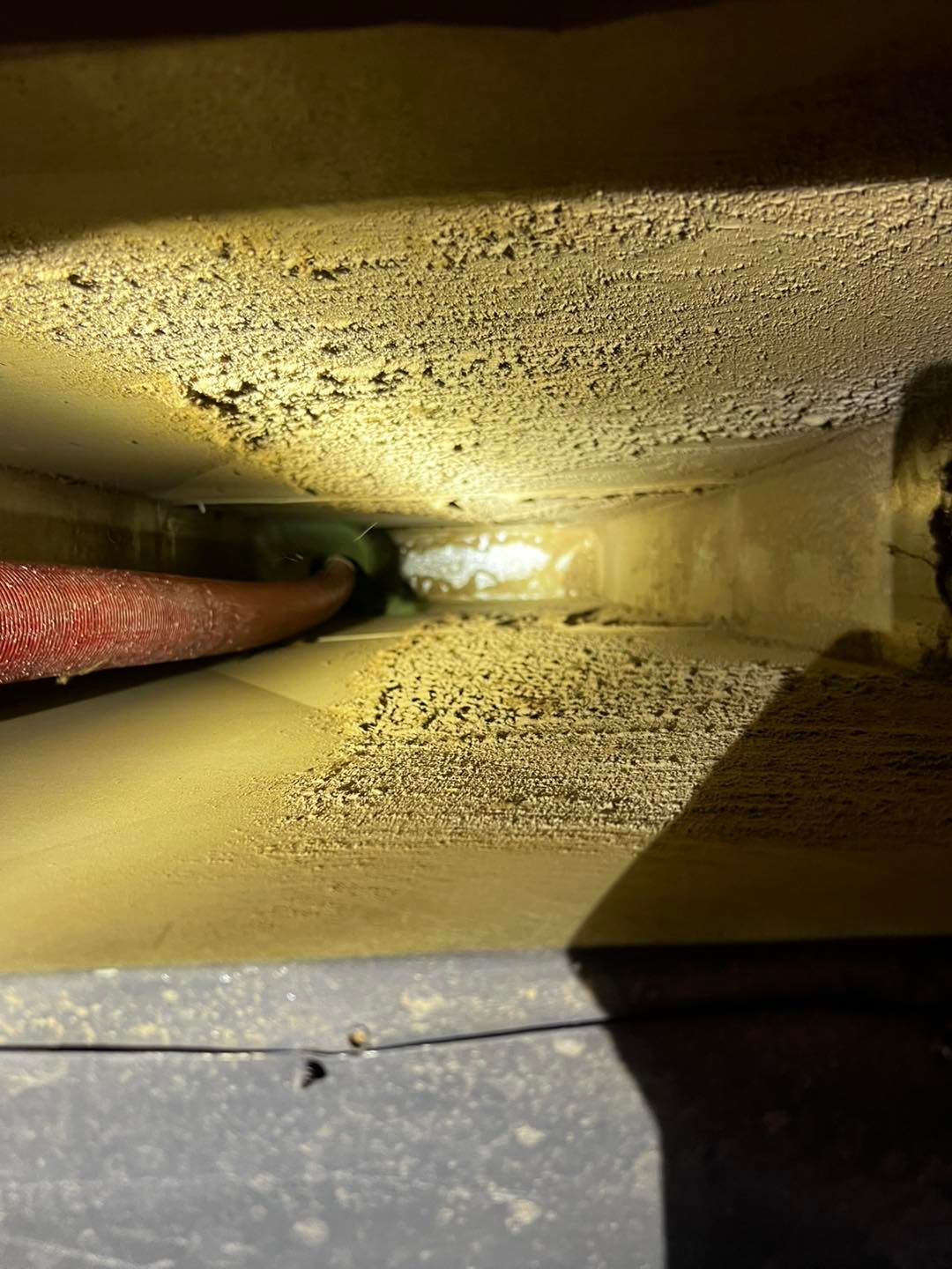 Close-up inside a dusty yellow vent with a red finger pointing toward a bright opening.