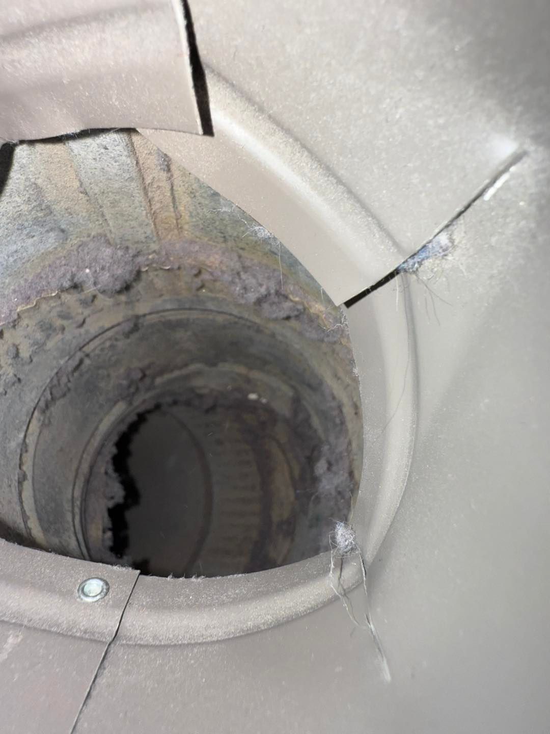 Close-up of a cracked gray vent or pipe opening with a torn, damaged edge.