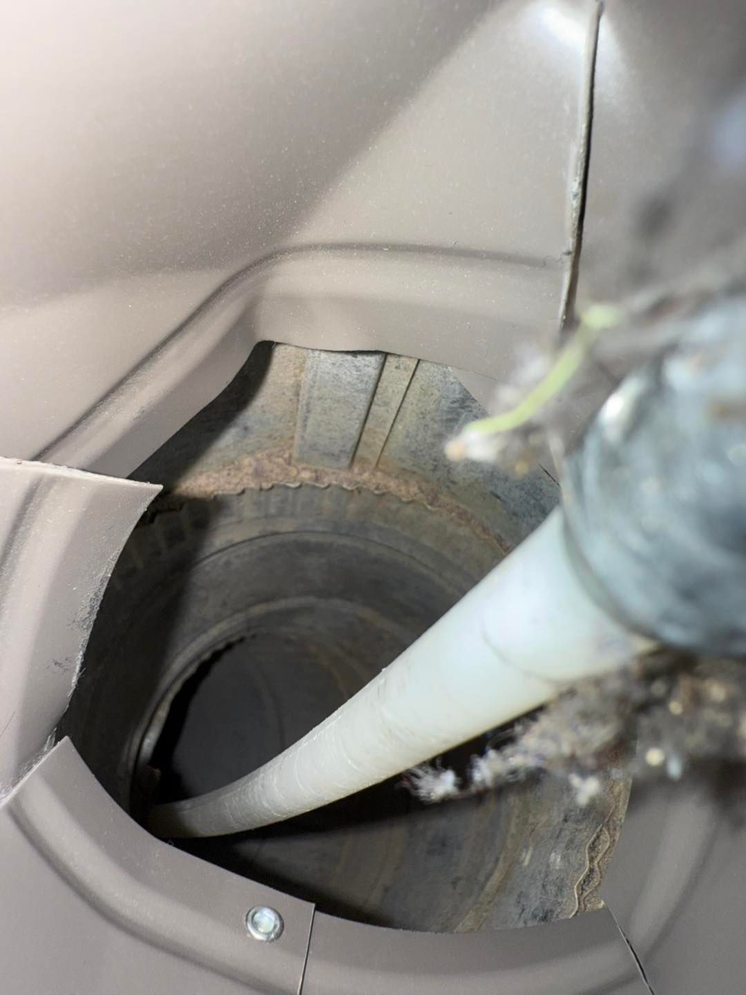 White hose inserted into a round vent or pipe opening inside a dusty gray machine compartment