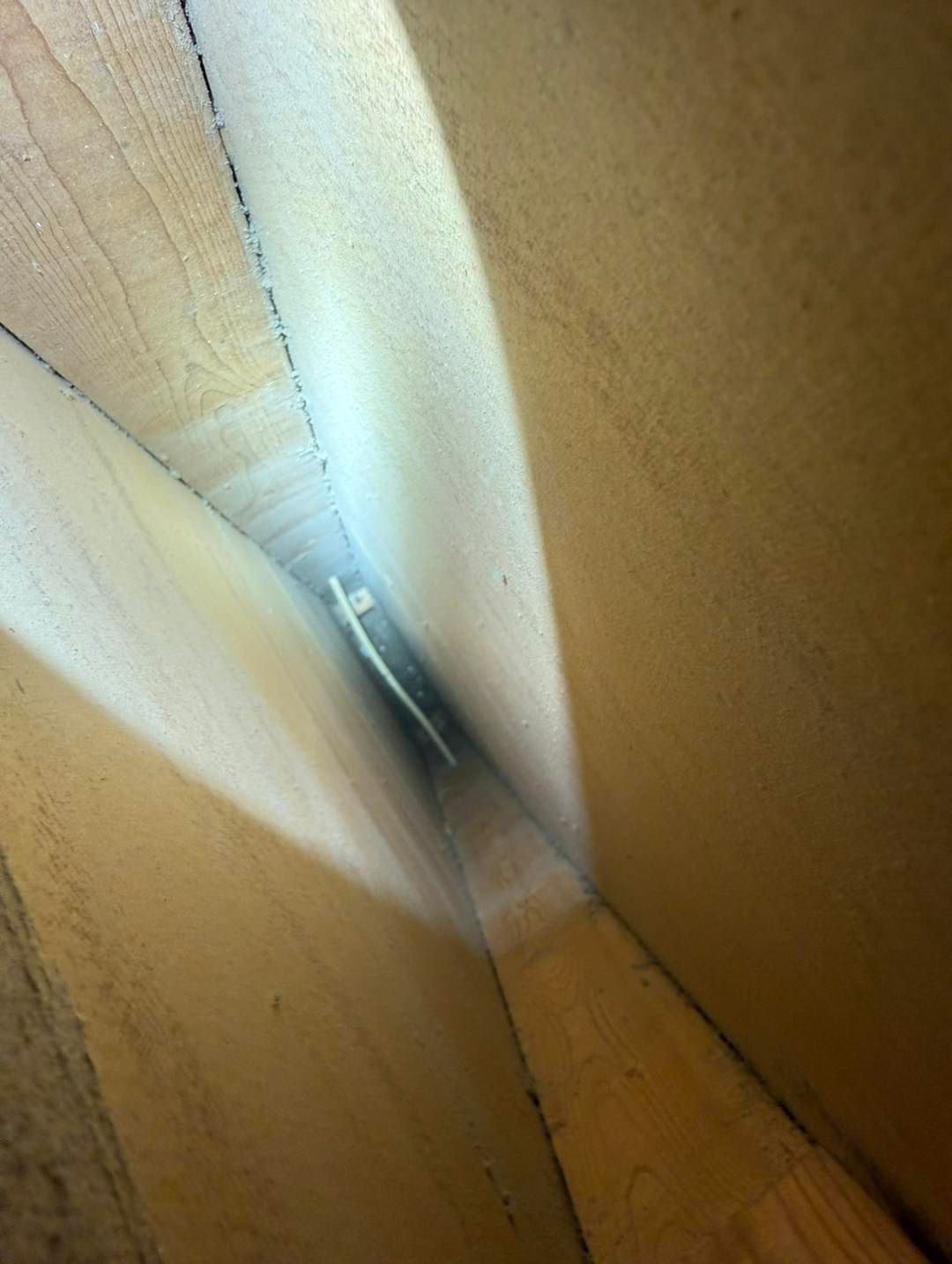 Close-up of a narrow gap between wooden panels with a blurry metal object inside.