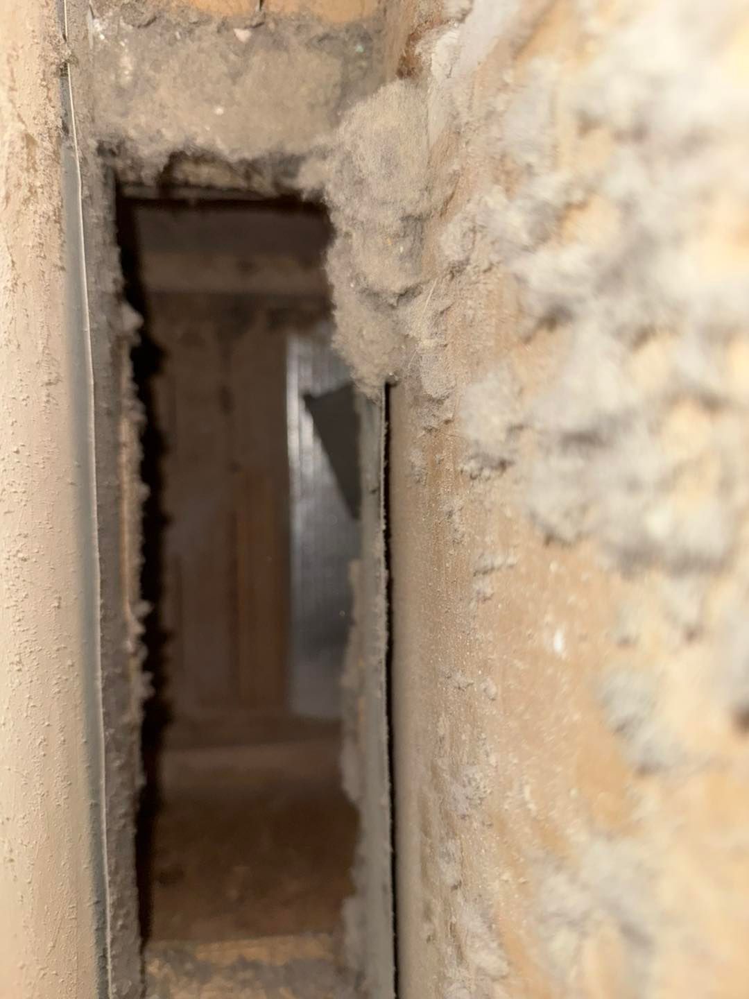 Narrow doorway in a dusty, unfinished wall, with a dim hallway visible beyond.