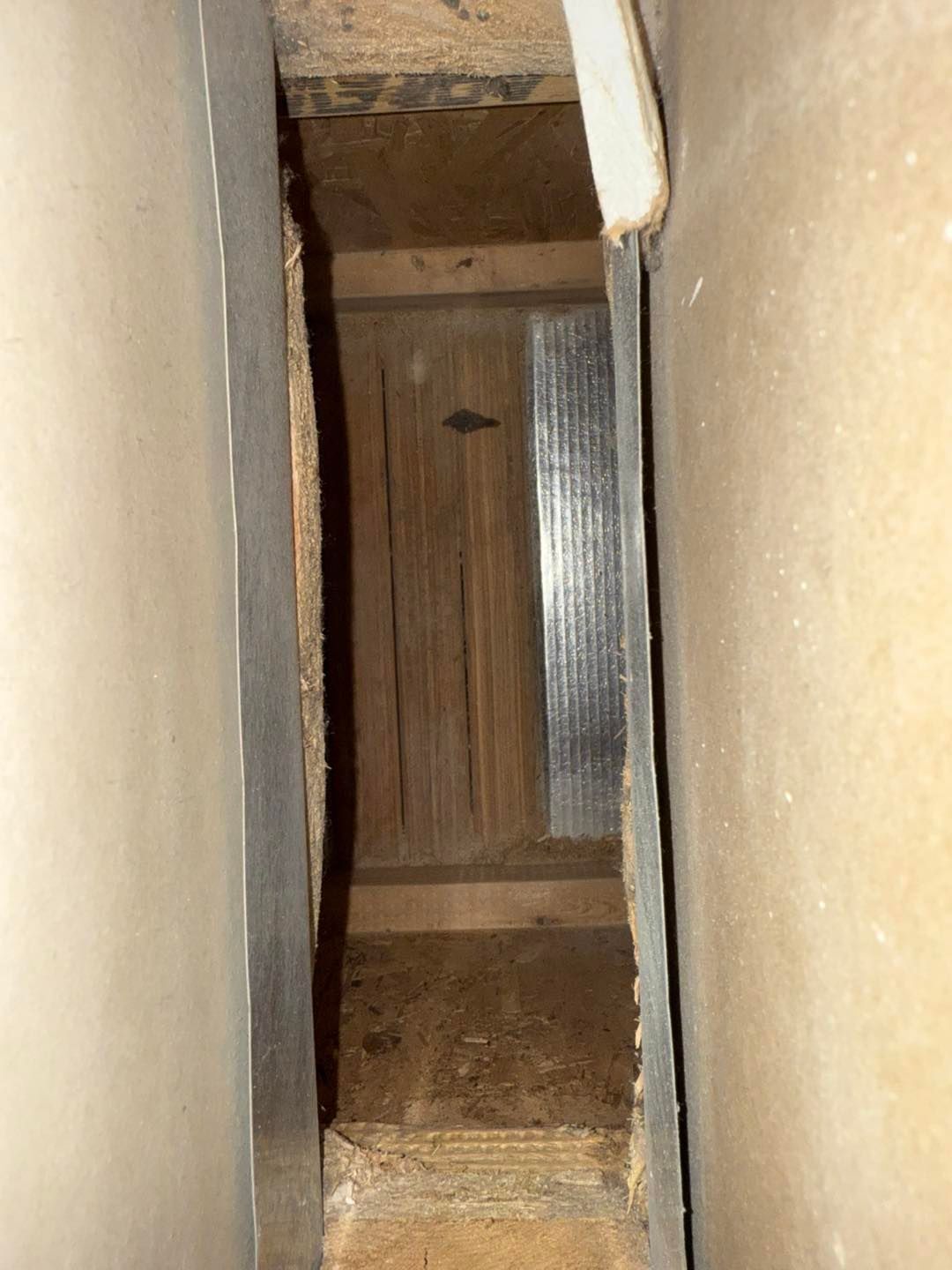 Narrow vertical gap between beige walls, showing a wooden surface and metal edge inside.