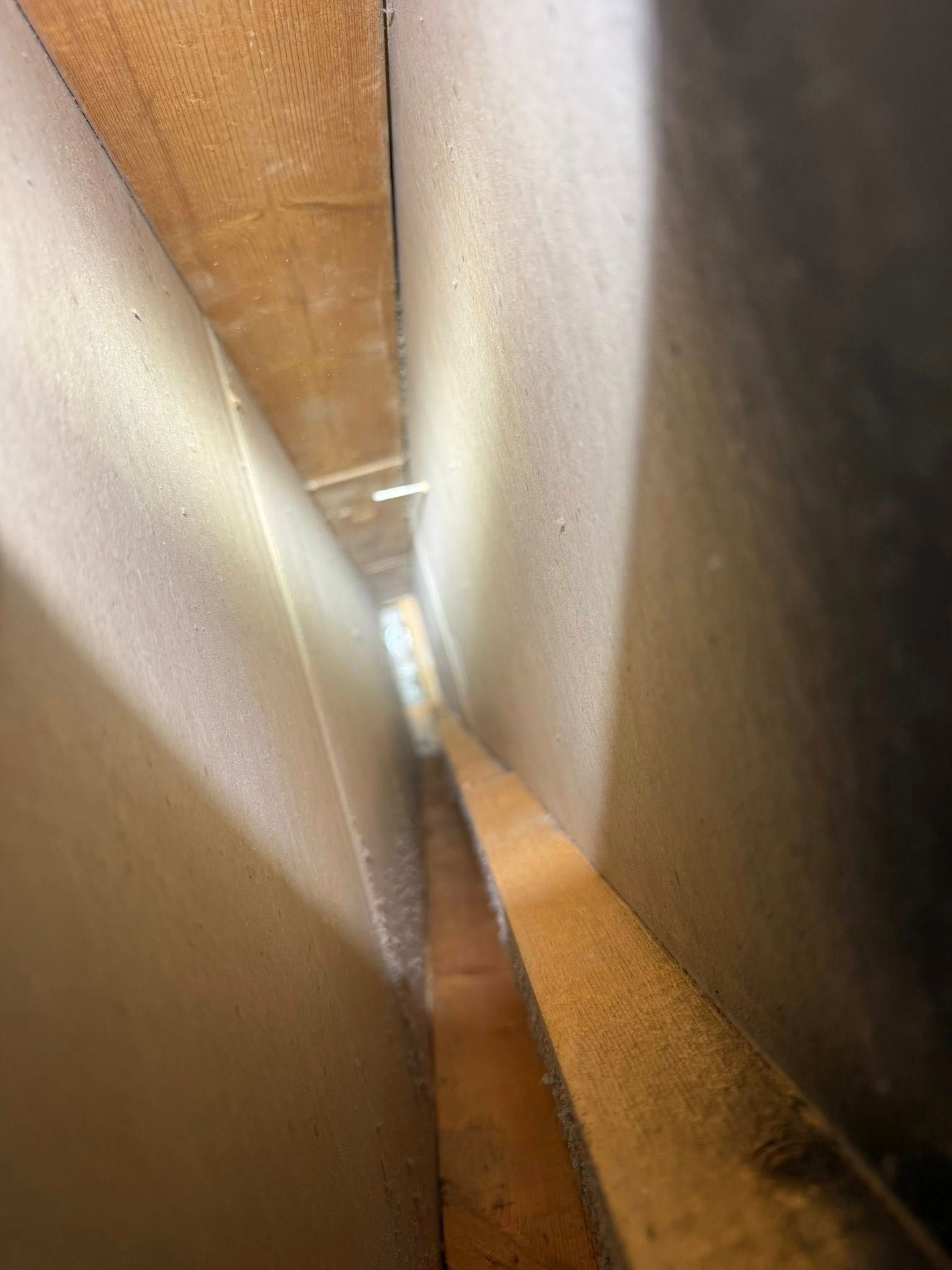 Narrow gap between two wooden surfaces with bright light at the far end