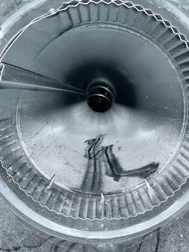 Top-down view inside a metal duct or funnel with a circular opening and ridged edge.
