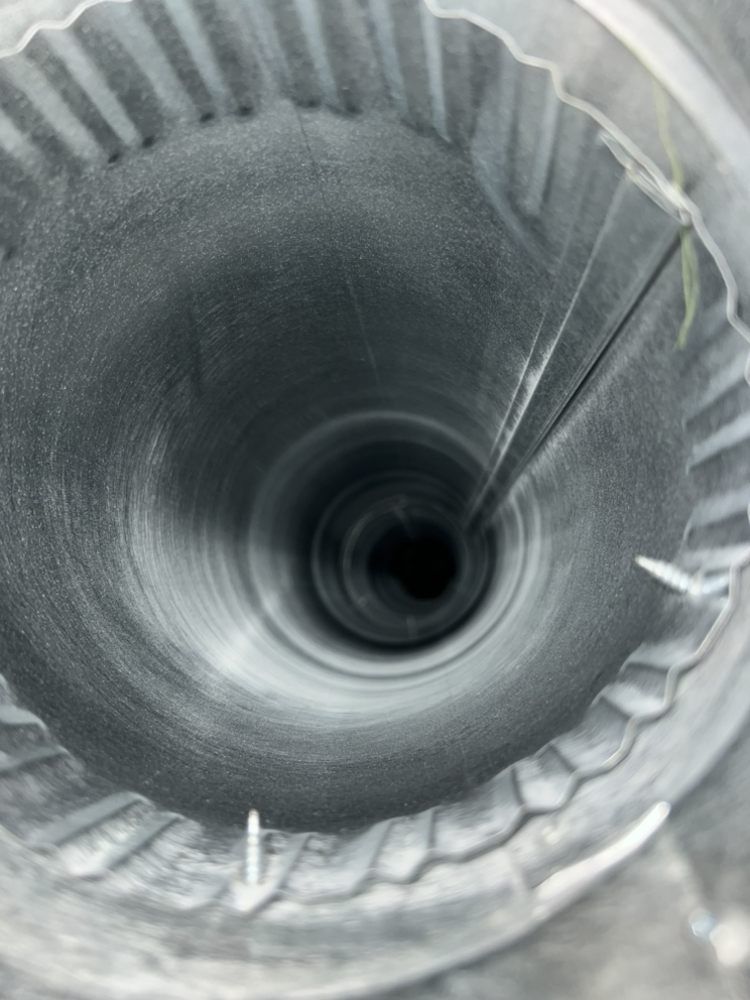 Top-down view into a narrow metal spiral duct with ridged, gray interior.