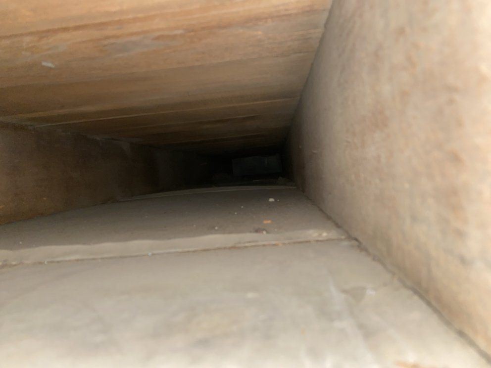 View inside a dark, narrow wooden duct or tunnel with beige walls and floor