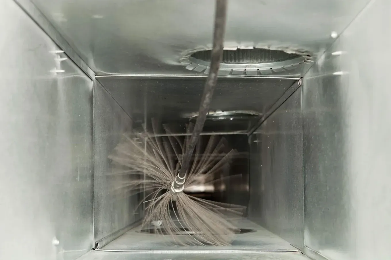 Inside a metal air duct, a cable hangs down over tangled wires and dust.