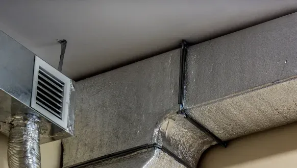 Metal HVAC ductwork with a wall vent near the ceiling corner