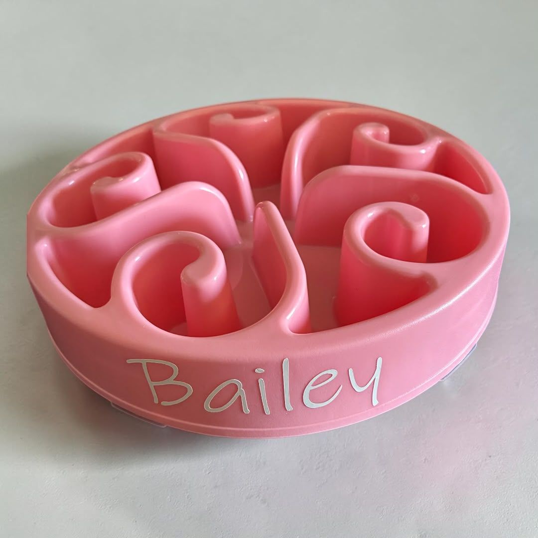 Roze ronde voerbak voor huisdieren met een slow-feeder ontwerp en reliëf, met het opschrift