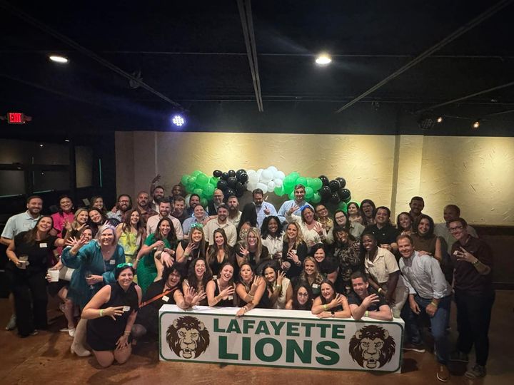 Large group posing indoors behind a “Lafayette Lions” banner and green-white balloon arch