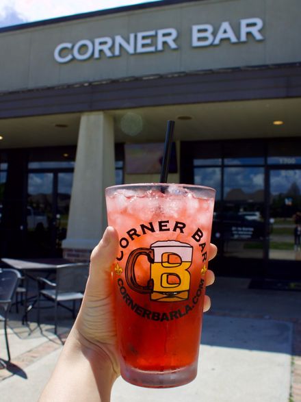 Hand holding red drink with ice in a Corner Bar cup outside the Corner Bar entrance