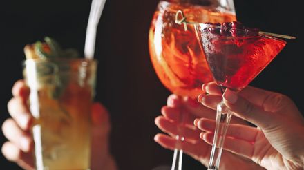 Hands toasting with colorful cocktails in martini glasses at a party