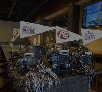Three football helmets on a table with pennants and a football team logo in the background.