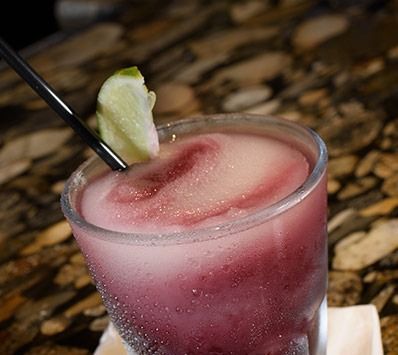 Pink frozen cocktail with a lime wedge and straw in a frosted glass