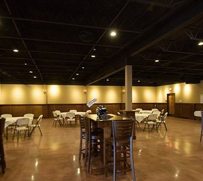 Empty banquet hall with round tables, chairs, and a polished floor under warm ceiling lights