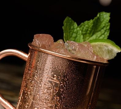 Copper mug with crushed ice, mint leaves, and a lime wedge on top, likely a cocktail