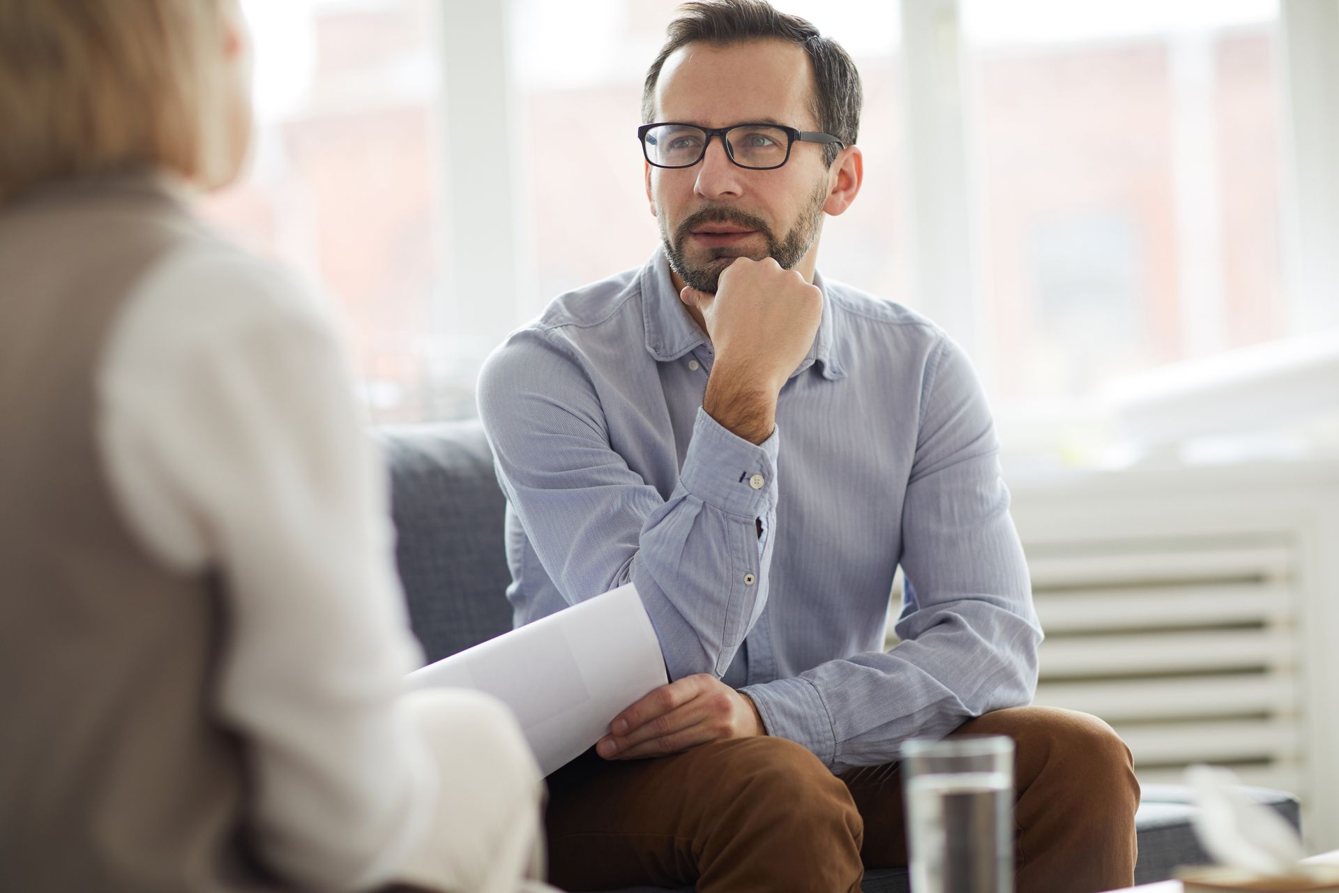 A man with glasses is sitting on a couch talking to a woman.