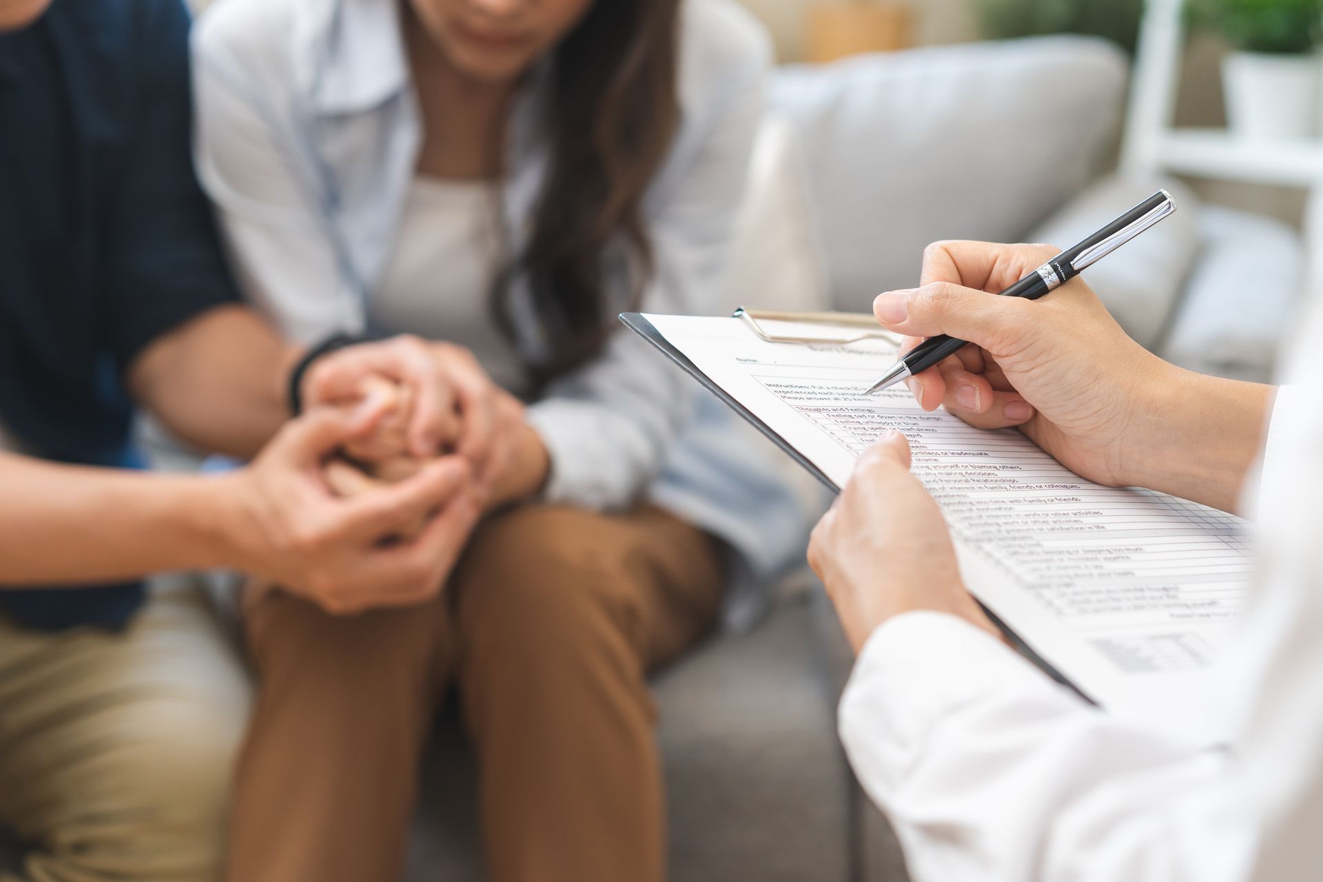 A man and a woman are sitting on a couch while a doctor writes on a clipboard.