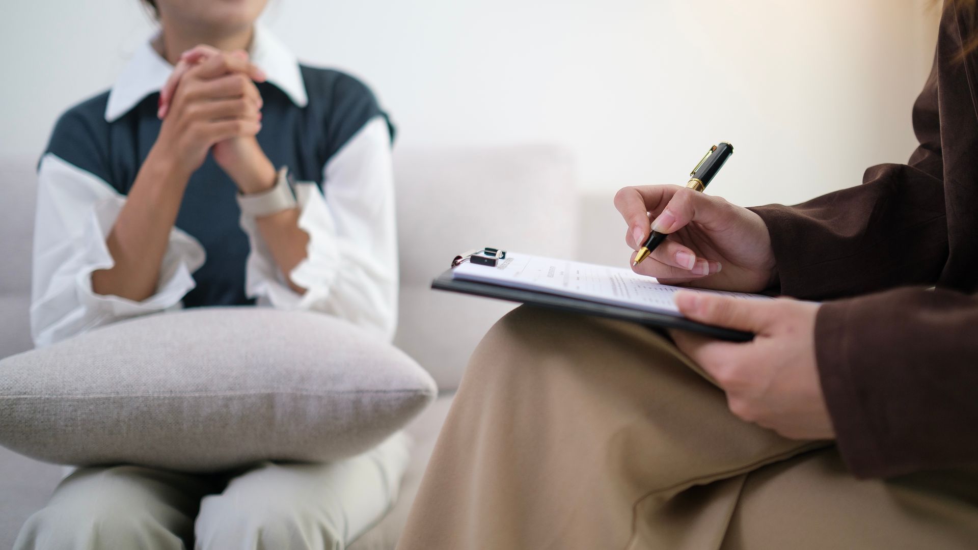 A woman is sitting on a couch talking to a man who is holding a clipboard.