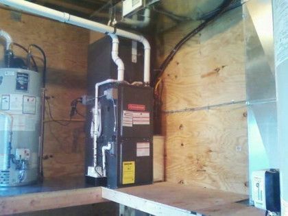 Furnace and water heater in a wooden-walled utility room. White pipes and ductwork are visible.