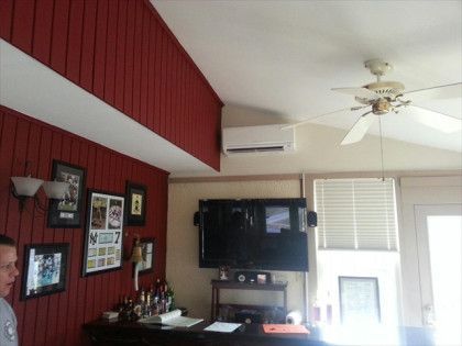 Living room with red wall, TV, air conditioner, ceiling fan, and a person.