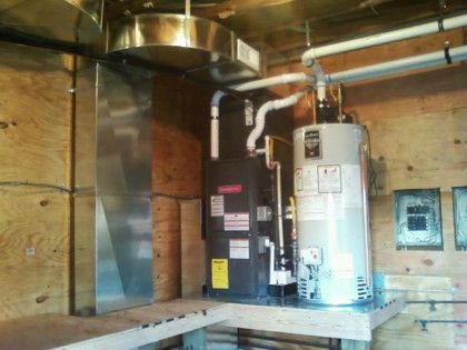 Water heater setup in a room with plywood walls. Includes an electric water heater, gas water heater, and ductwork.