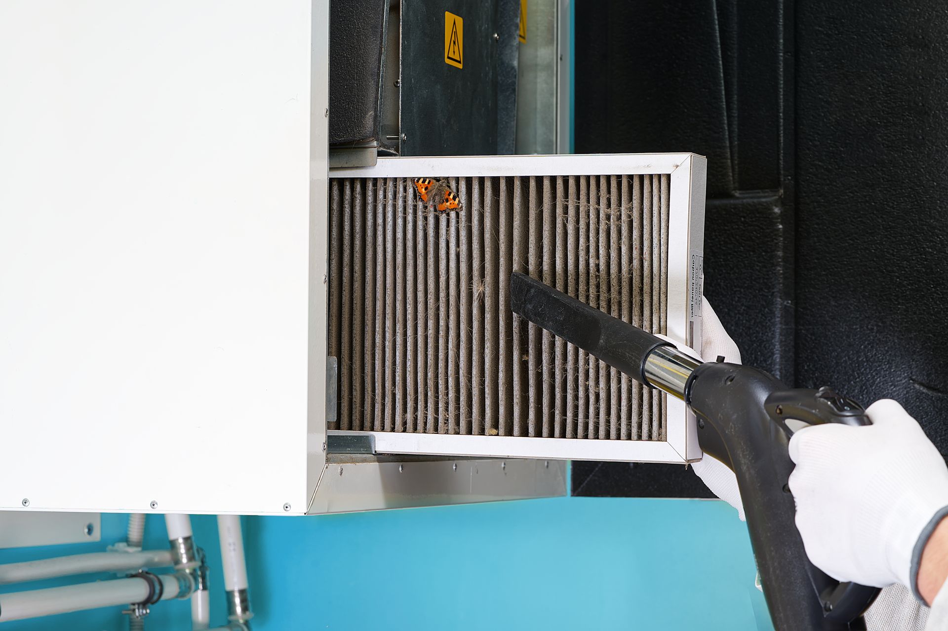 Person vacuuming a dusty air filter in a machine compartment