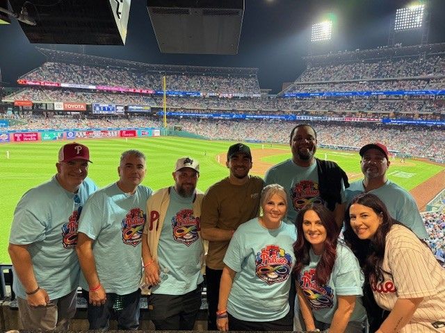 Group of fans in matching light blue shirts posing at a baseball stadium at night
