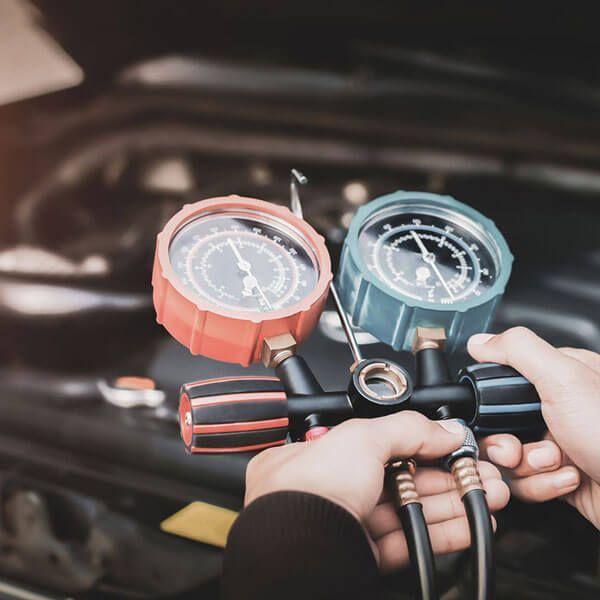 Hands holding red and blue automotive gauges with hoses attached in front of an open engine bay