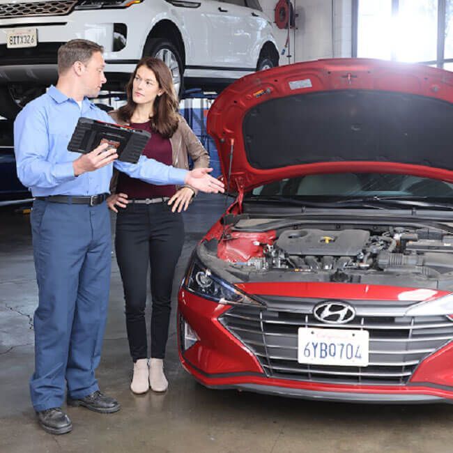 Mechanic and customer discussing a red Hyundai with its hood open in a garage