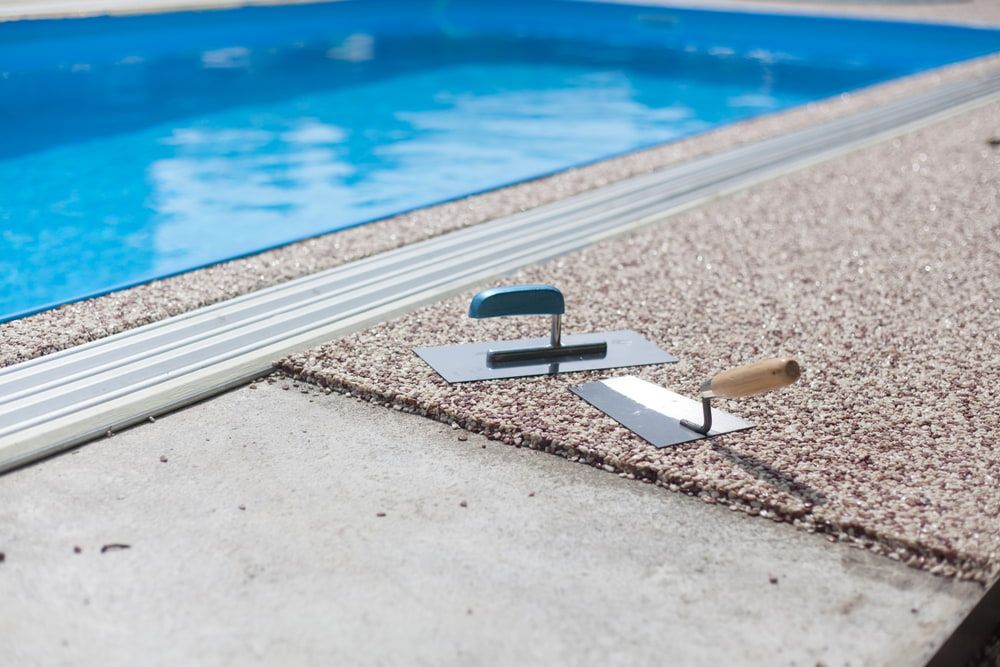 A Trowel Is Laying On The Ground Next To A Swimming Pool — Tuncote Concrete Constructions in Nelson Bay, NSW