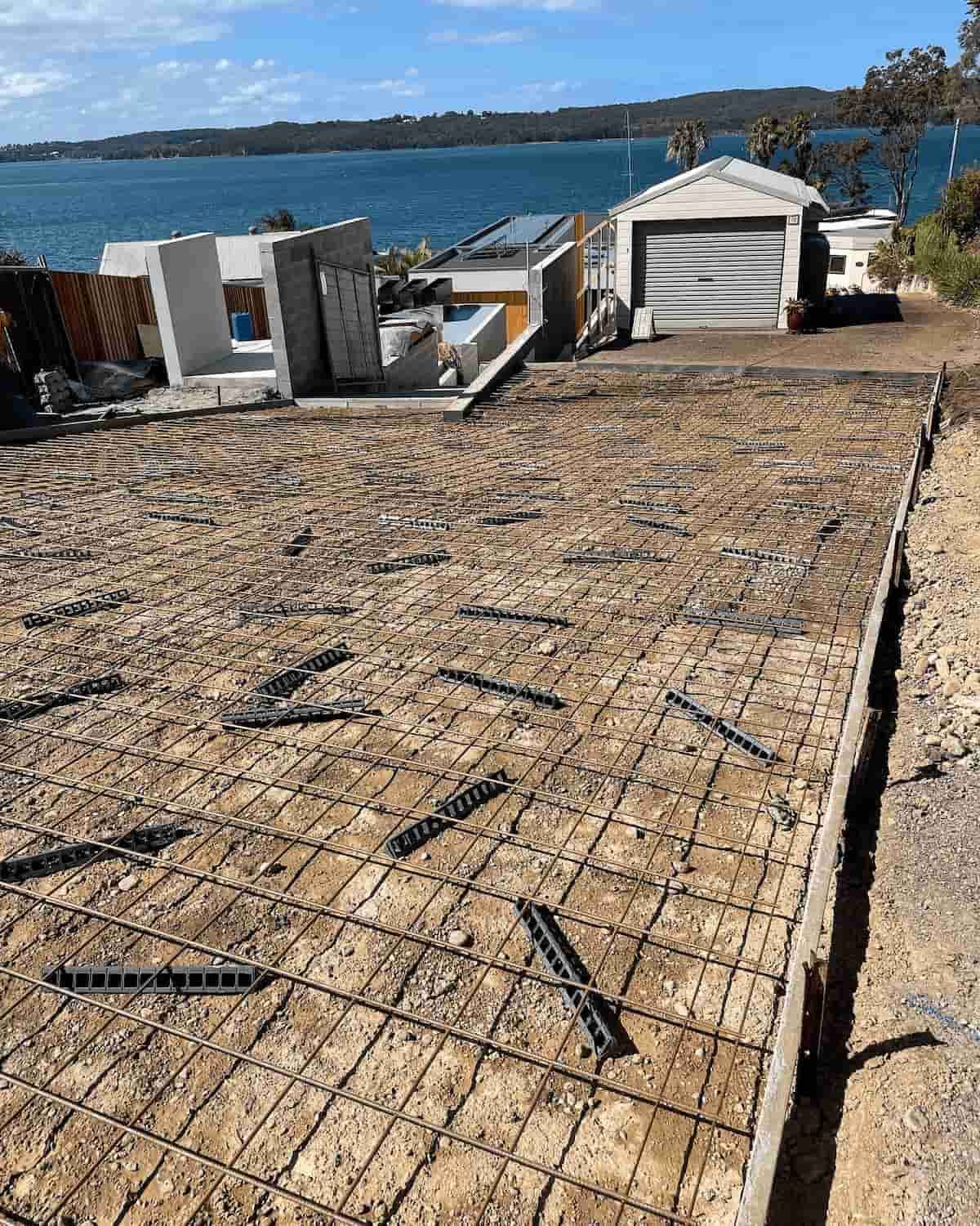 A Concrete Driveway Is Being Built In Front Of A House Next To A Body Of Water — Tuncote Concrete Constructions in Nelson Bay, NSW