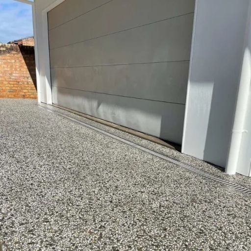 A Garage Door With A Gravel Driveway In Front Of It — Tuncote Concrete Constructions in Nelson Bay, NSW