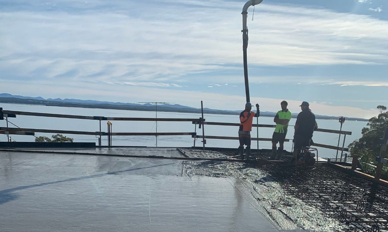 A Group Of People Are Standing On A Pier Overlooking A Body Of Water — Tuncote Concrete Constructions in Anna Bay, NSW