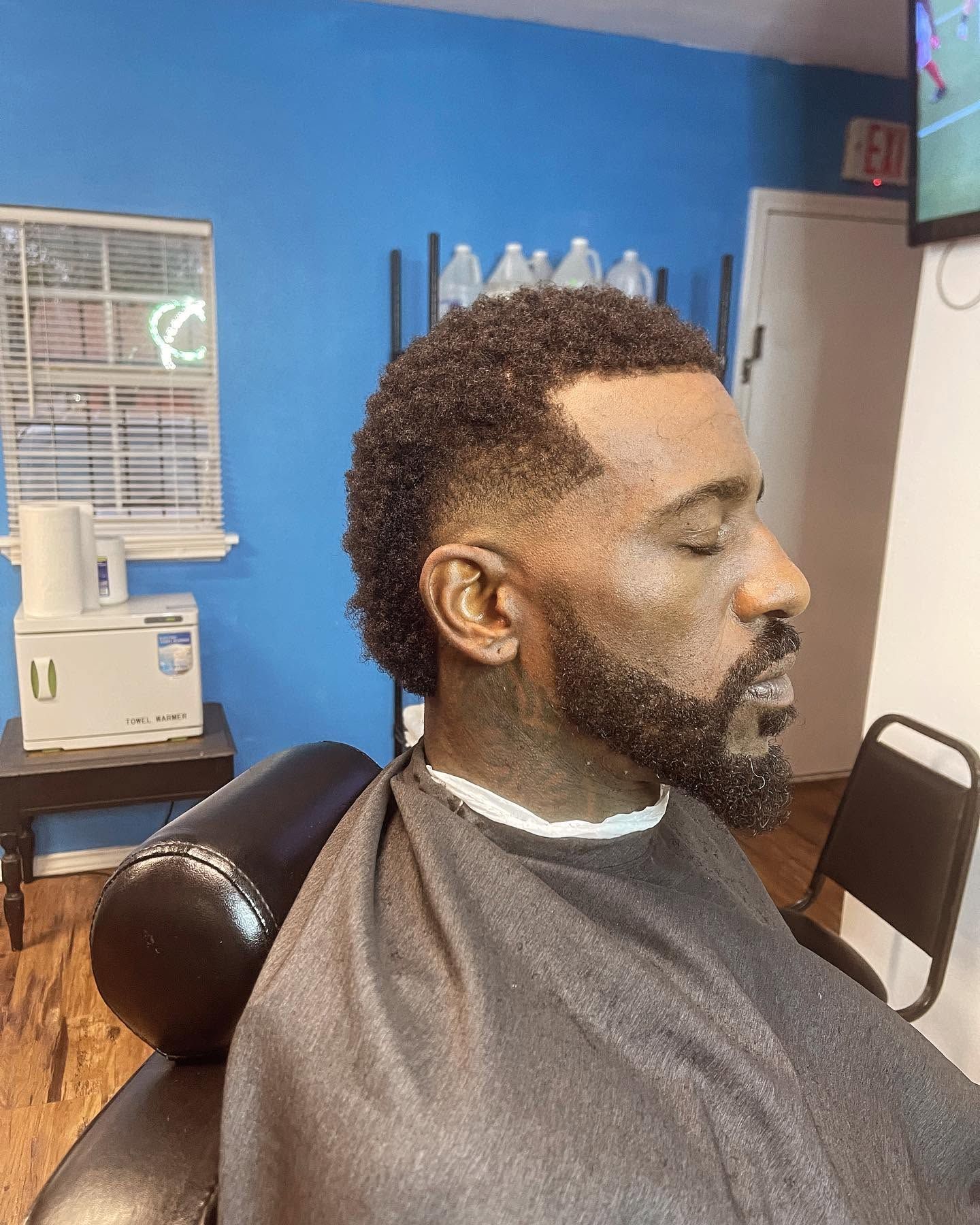 Man sitting in a barber chair with a fresh haircut and beard trim in a barbershop.