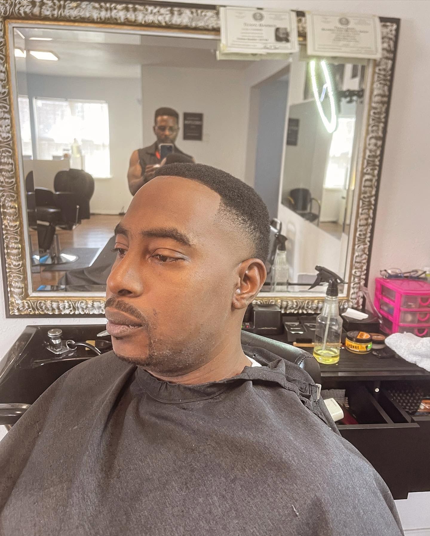 Man getting a fresh haircut in a barbershop chair, with a mirror and grooming tools behind him.
