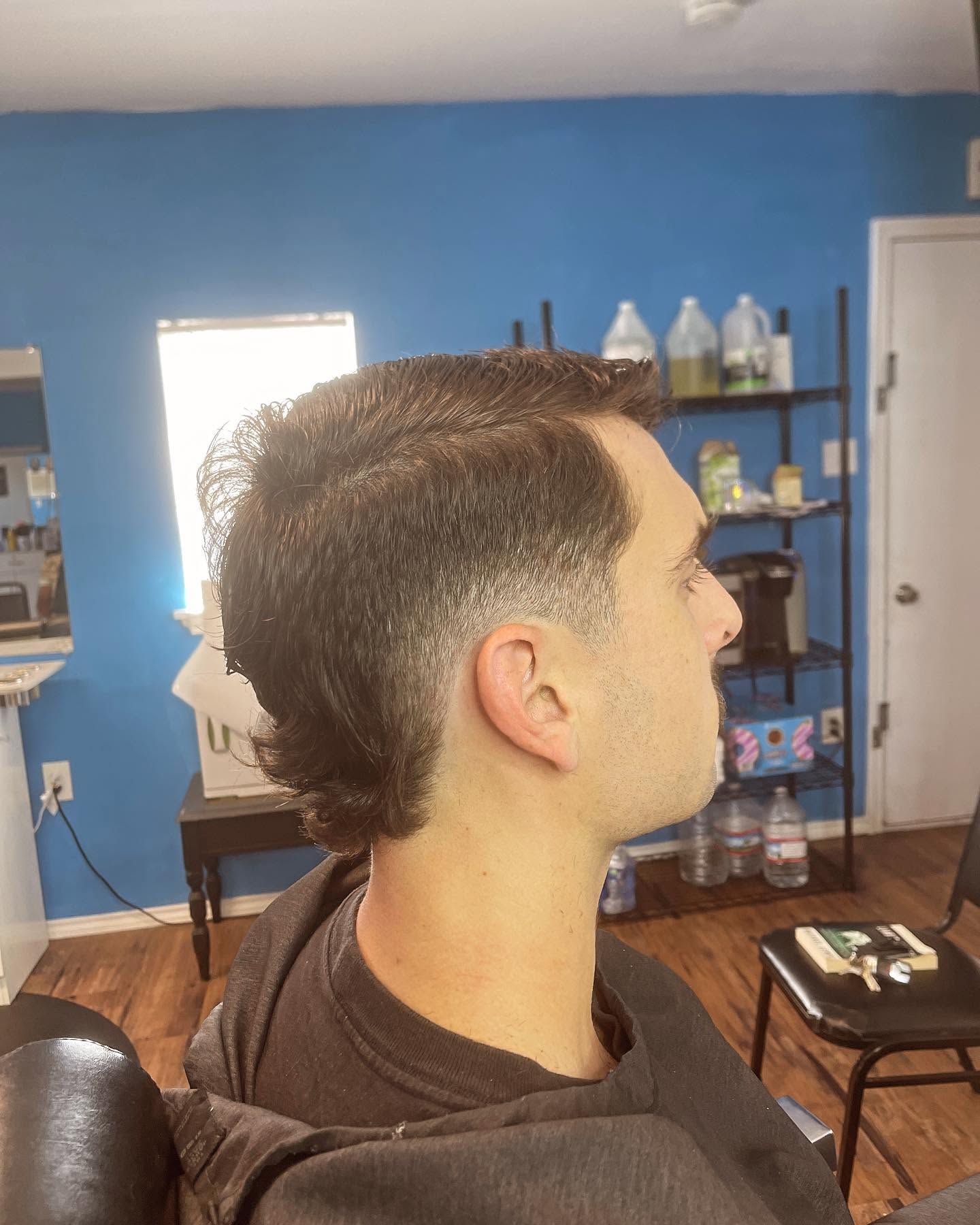 Side profile of a person with a short faded haircut in a blue barbershop interior.