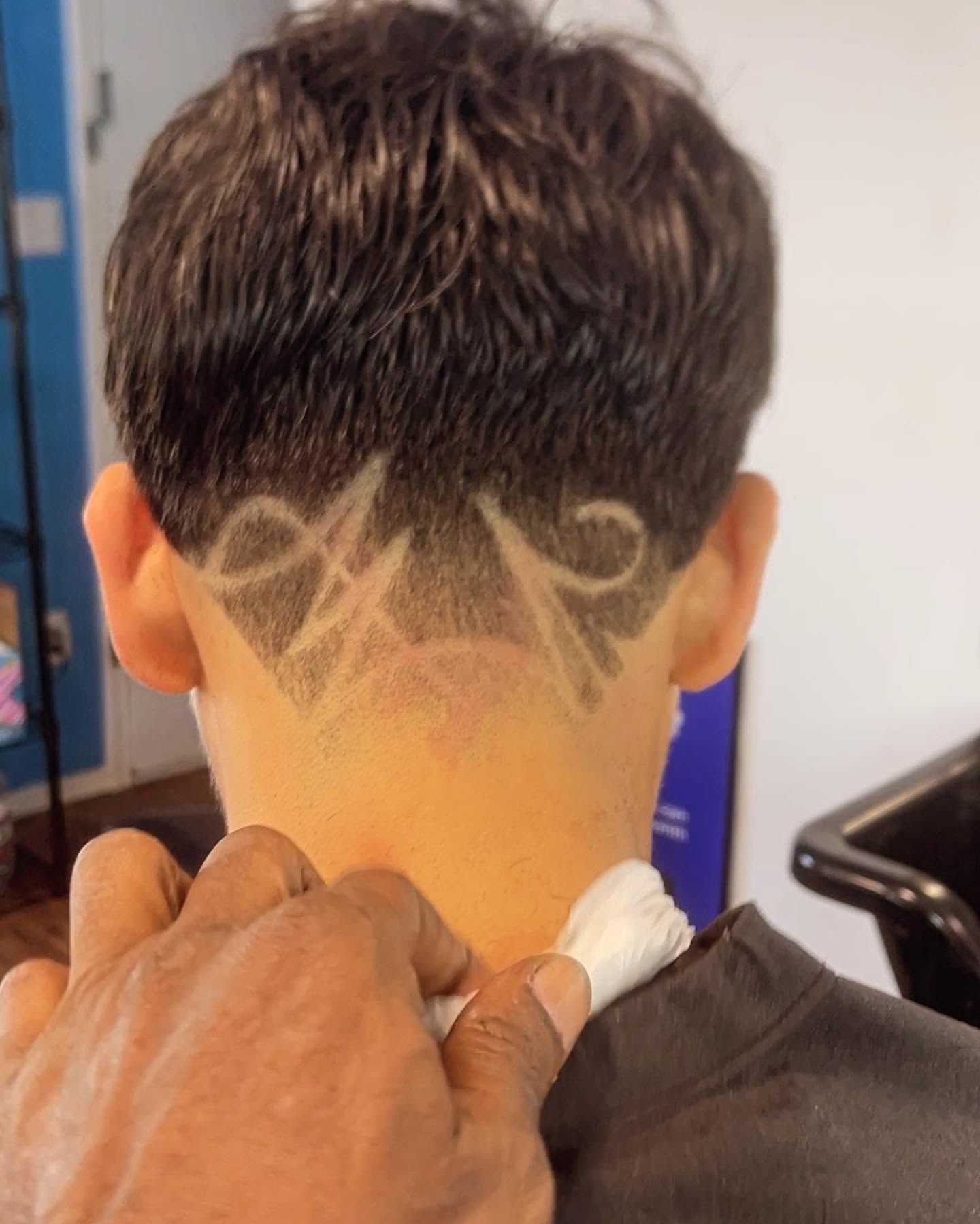 Barber shaping a zigzag design into the back of a short haircut with clippers