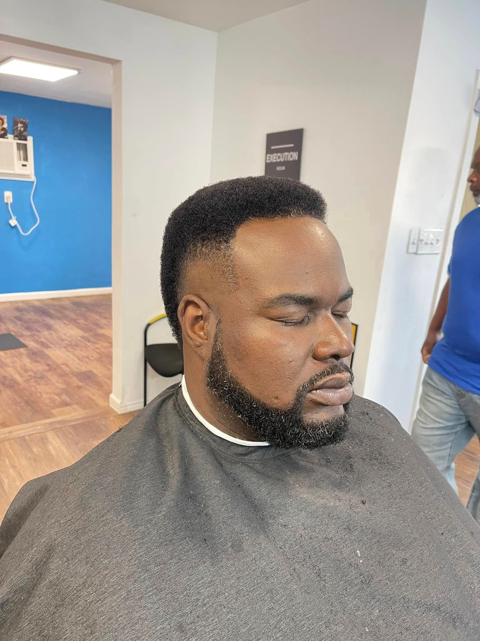 Man getting a haircut in a barbershop, with a fresh fade and dark cape.
