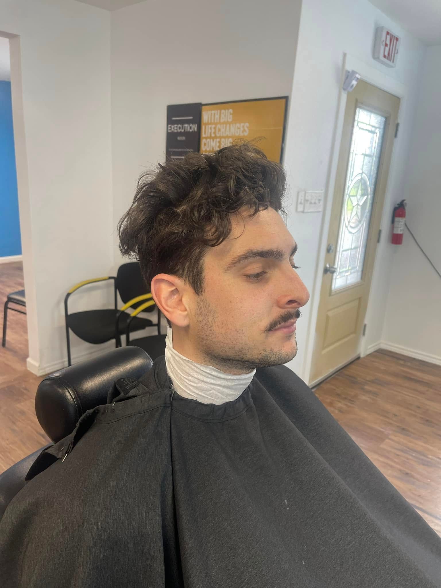 Person seated in a barber chair with a black cape and white neck strip in a salon.