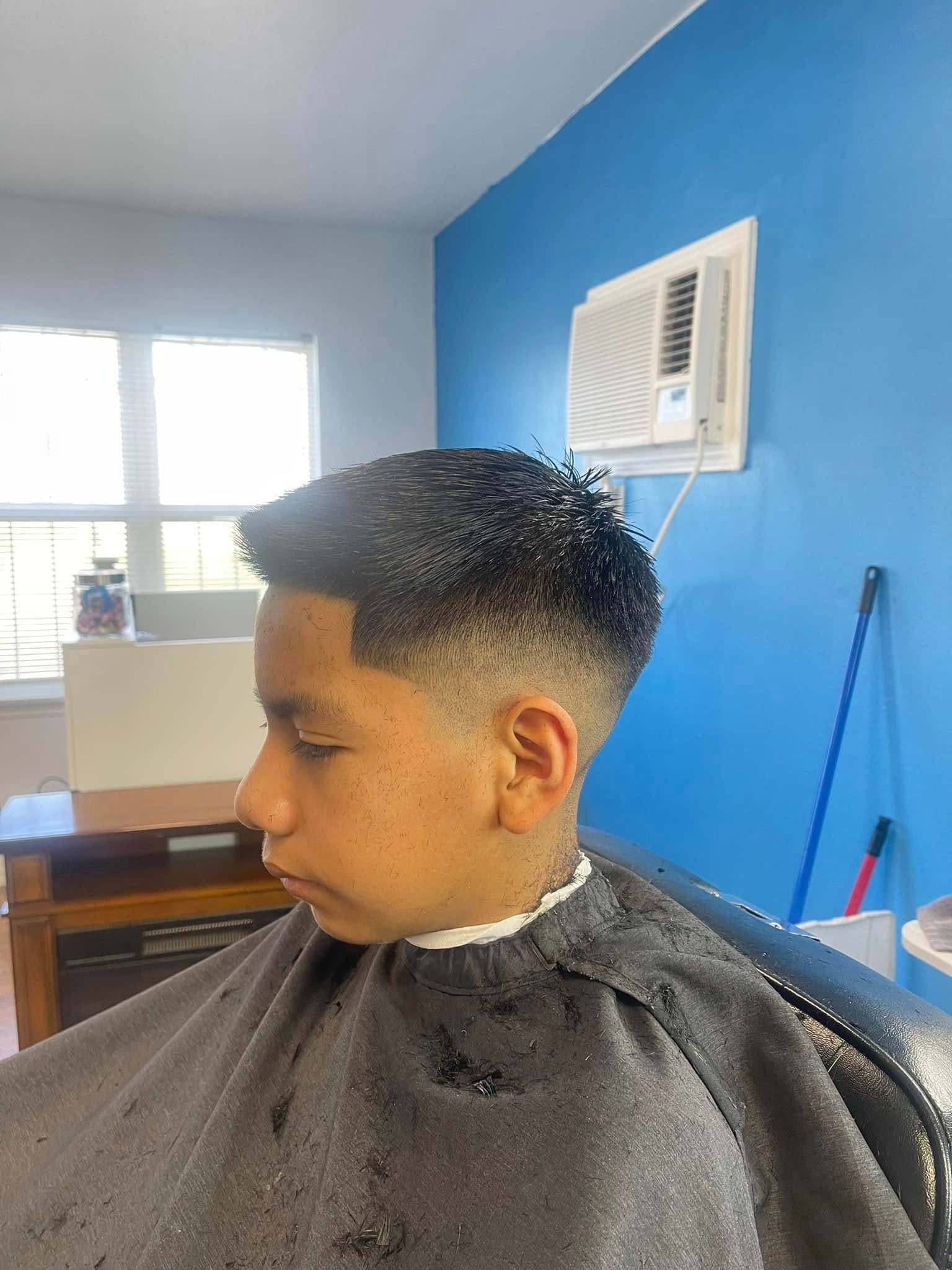 Child getting a haircut in a barbershop, with a blue wall and window in the background.