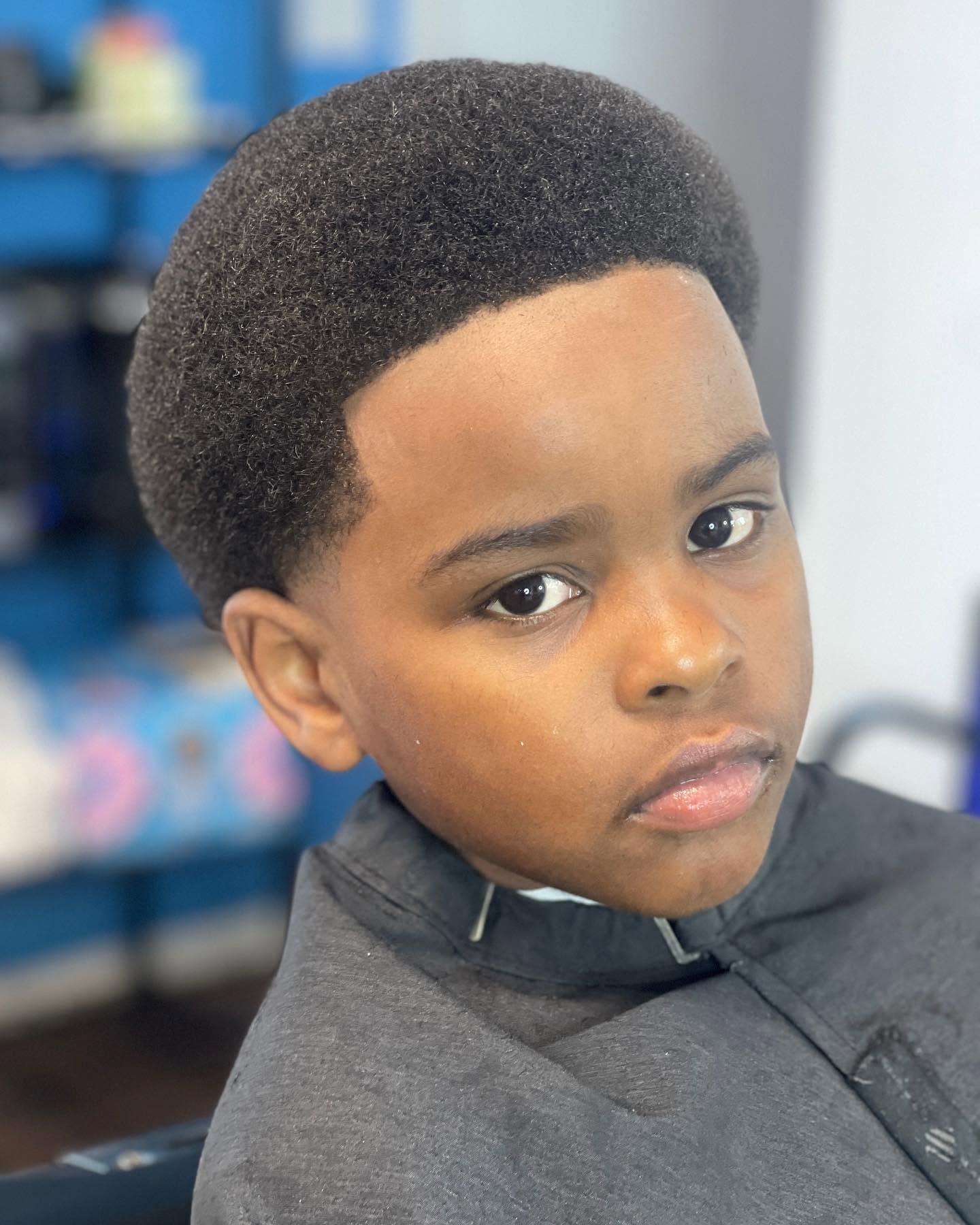 Portrait of a child with a rounded afro, wearing a dark top and looking at the camera
