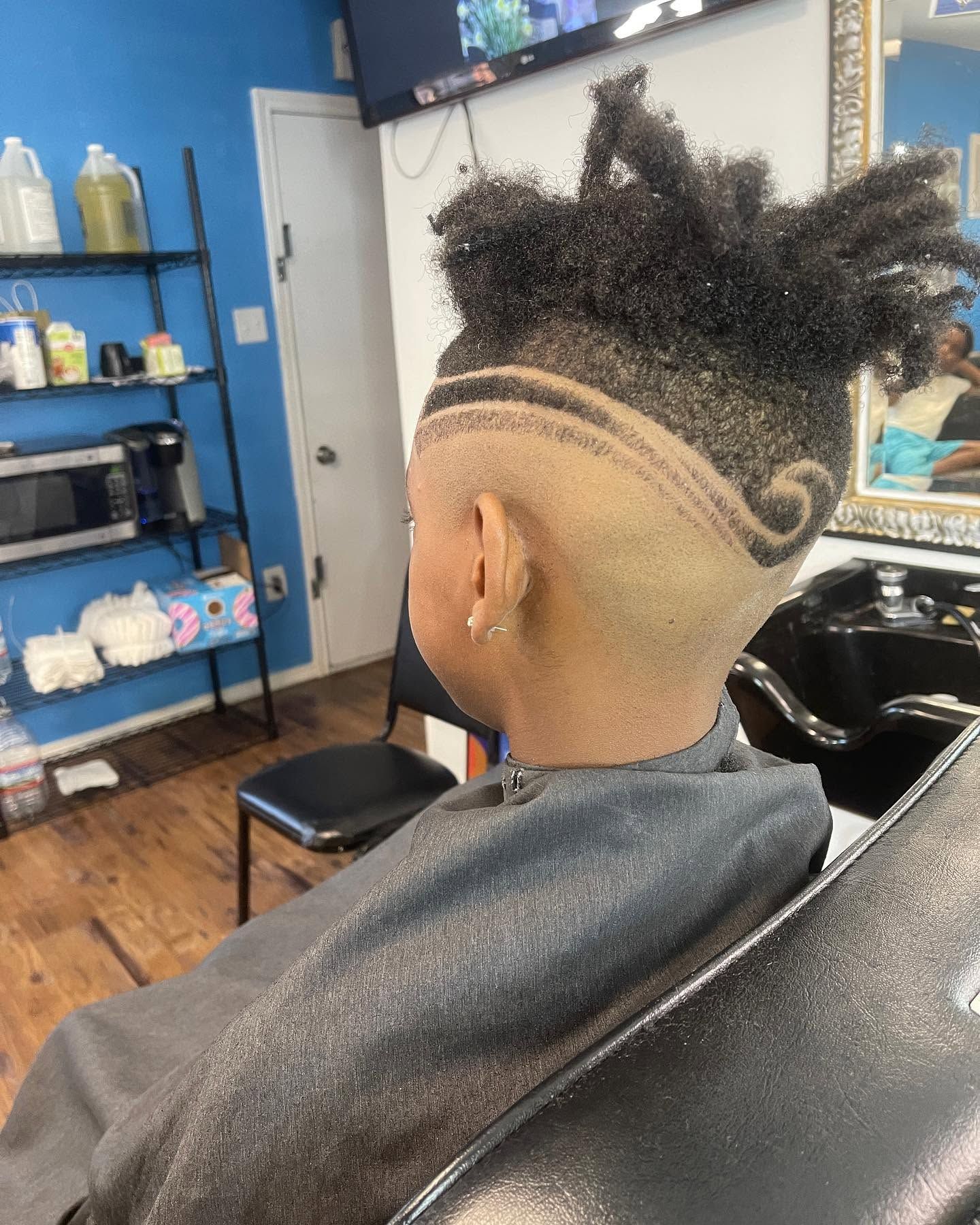 Side view of a shaved hairstyle with swirl designs in a barbershop chair.