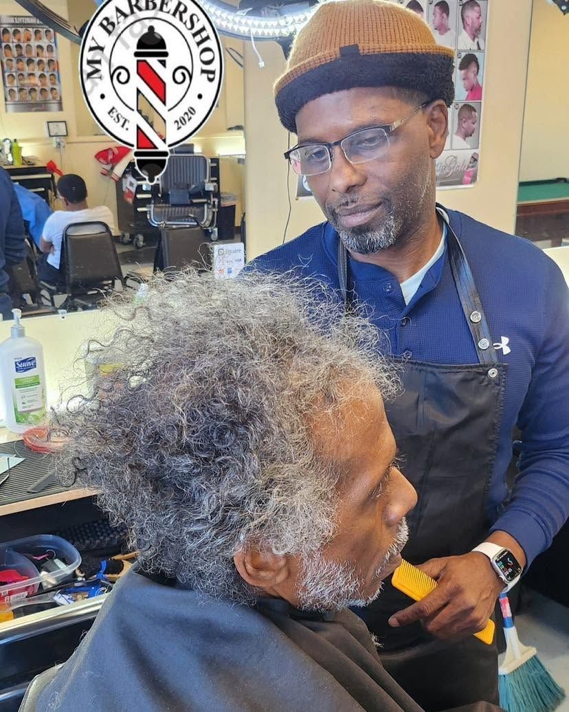 Barber trimming a customer’s hair in a salon, with mirror and tools visible.