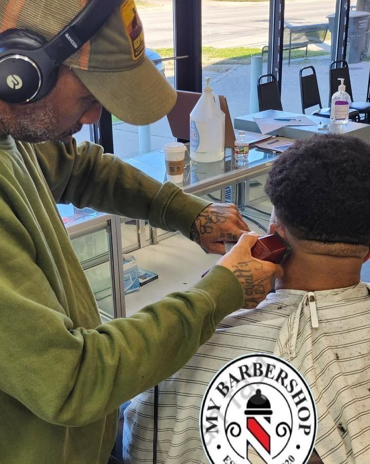 Barber trimming a client’s hair in a barbershop, wearing headphones and a cap.