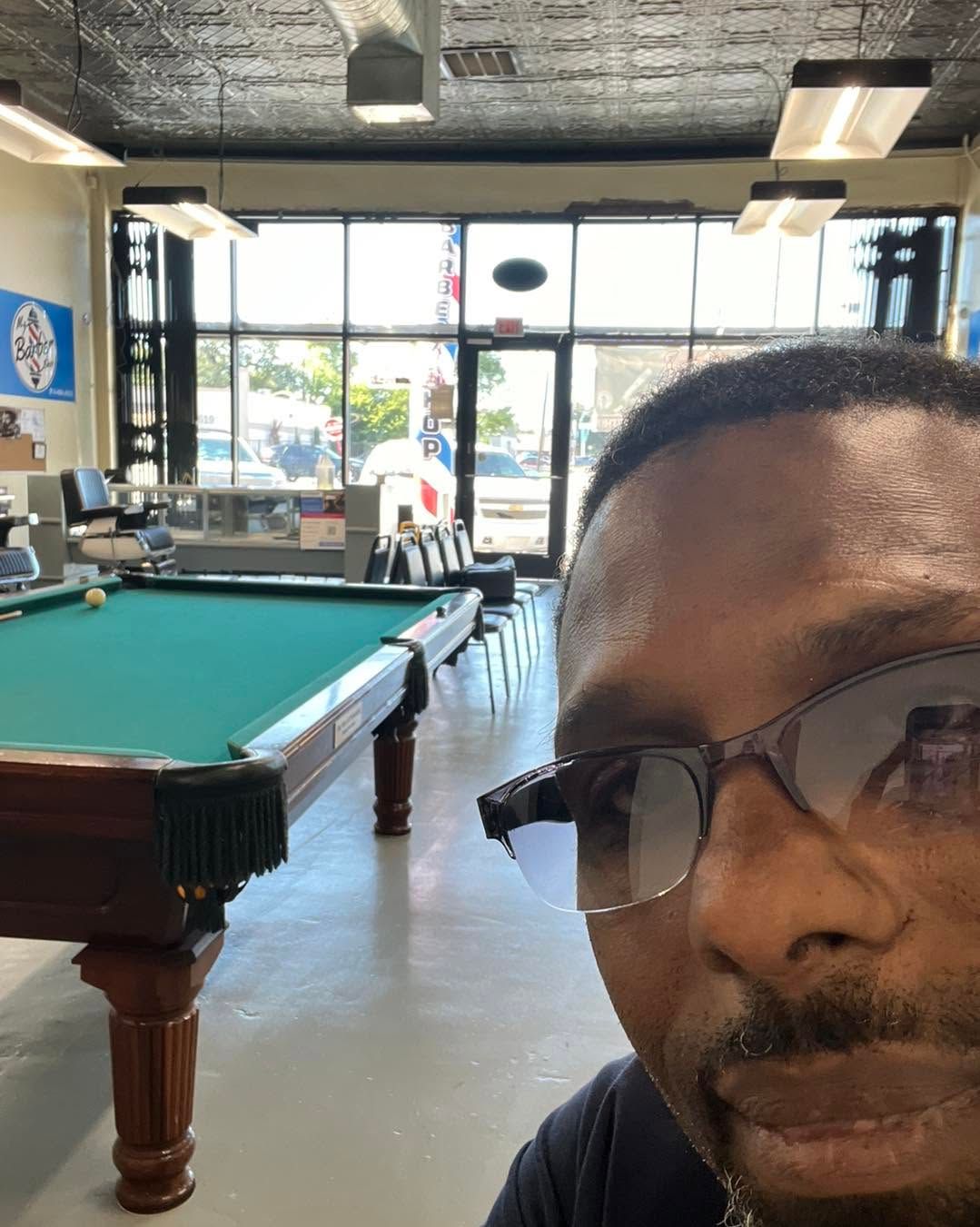 Selfie in a pool hall with a green billiards table and large windows in the background
