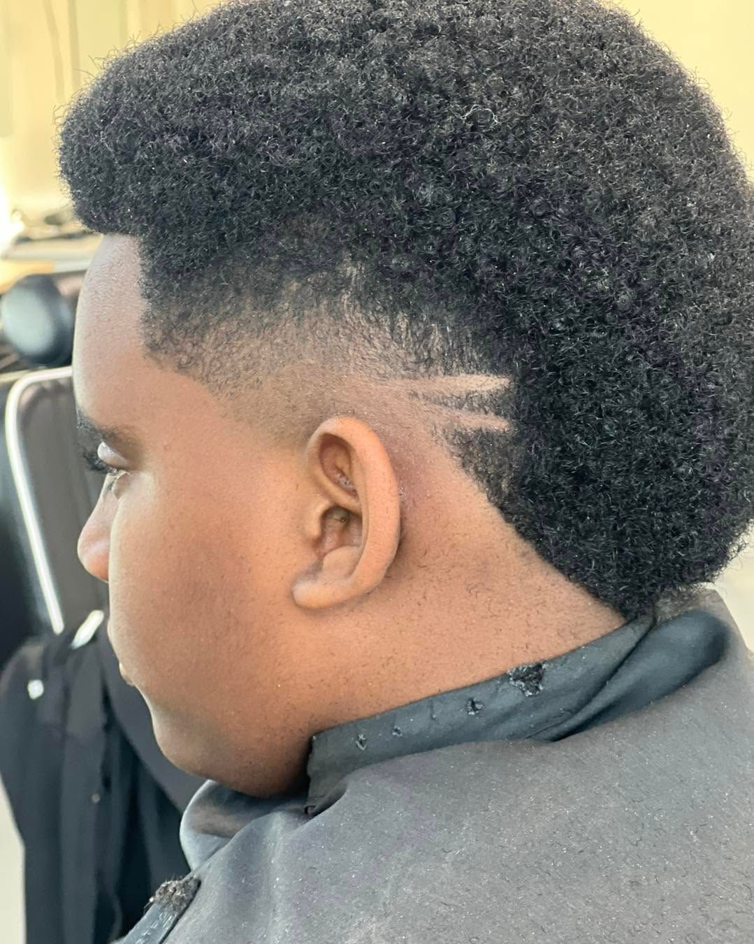 Side profile of a person with a faded haircut and natural hair, wearing a black cape in a barber chair.