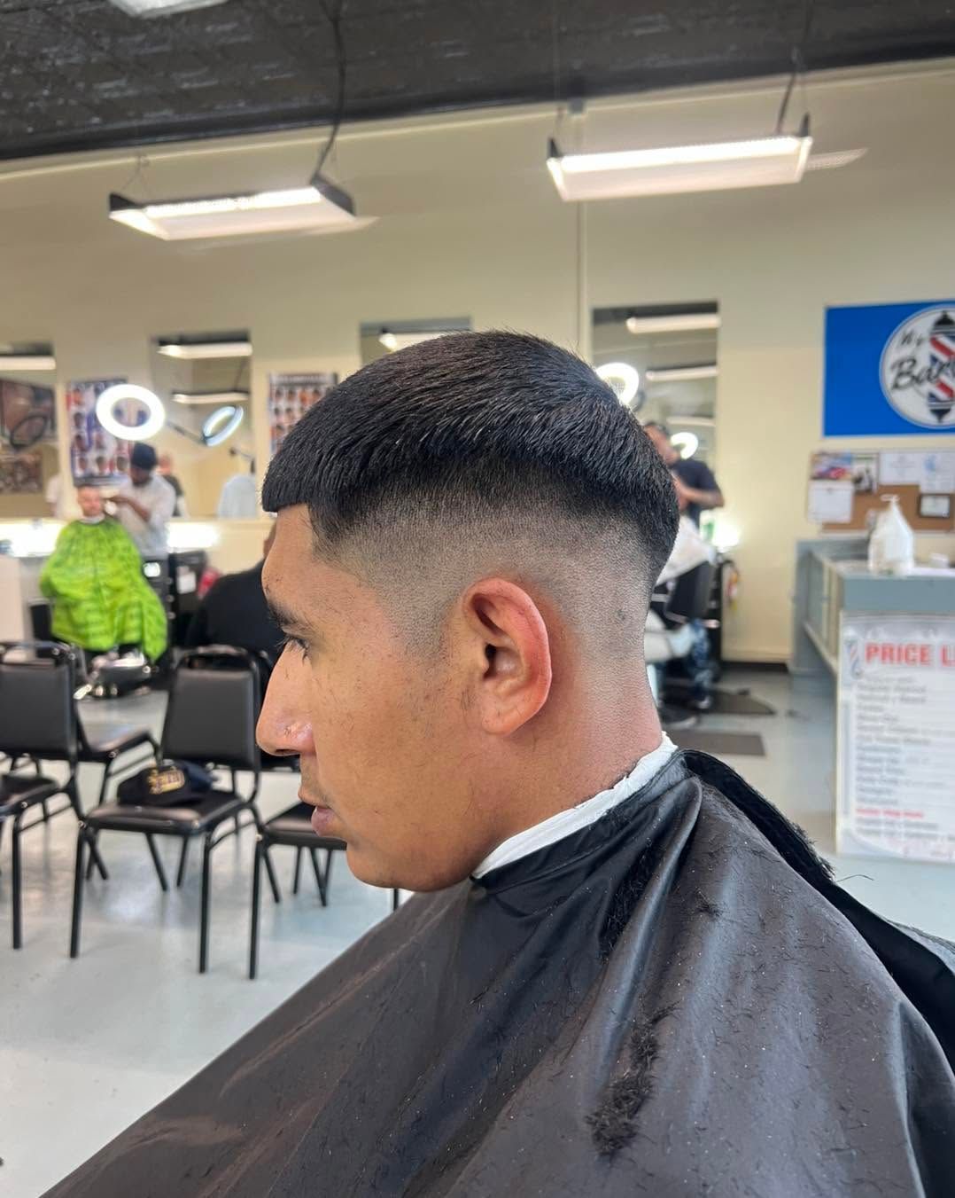 Side-profile haircut in a barbershop, with a dark cape and chairs and mirrors in the background