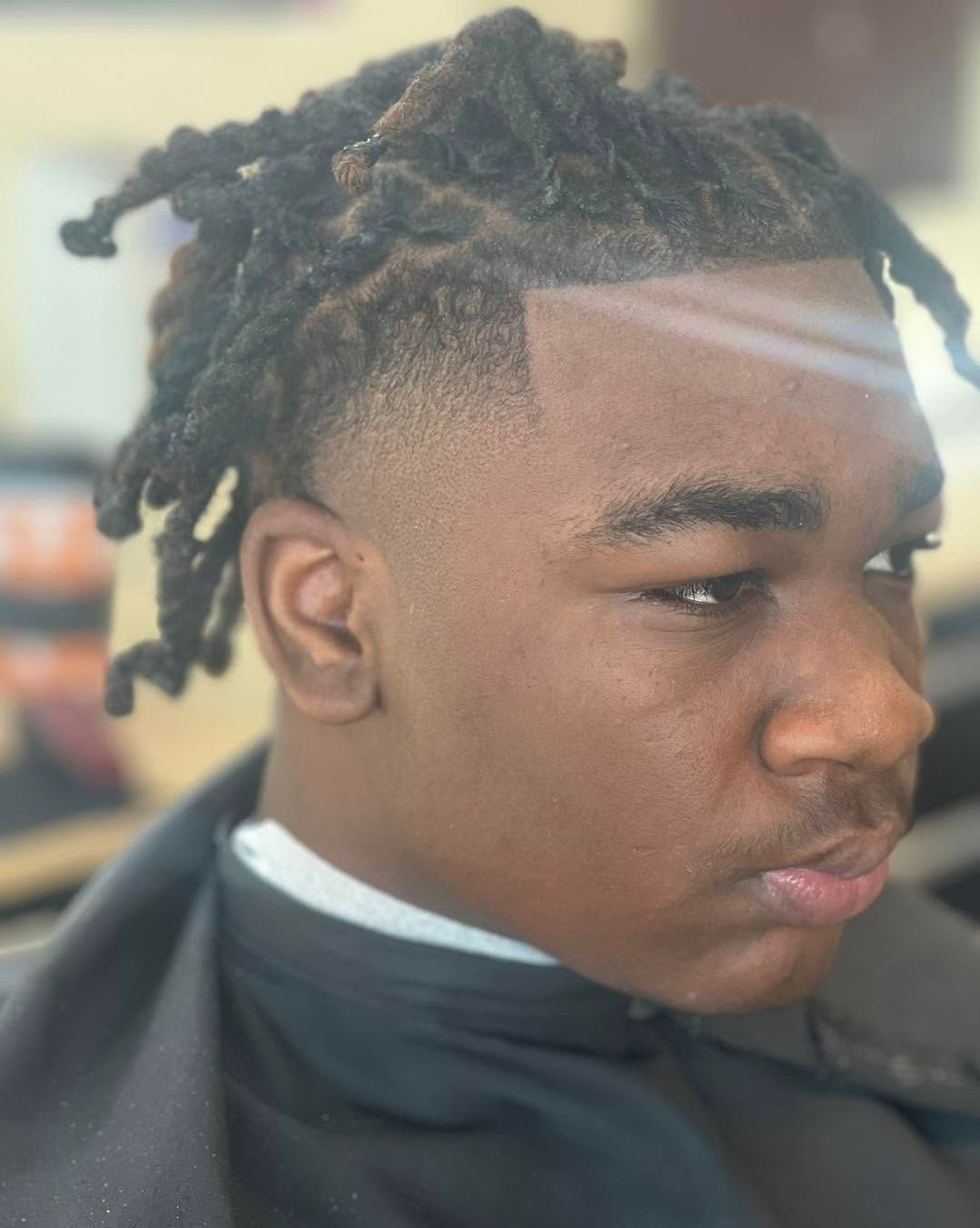 Close-up side profile of a person with twisted hair wearing a black barber cape, looking to the right.