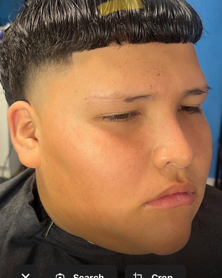 Close-up profile of a person with a sharp black haircut against a blue background, looking down with a neutral expression